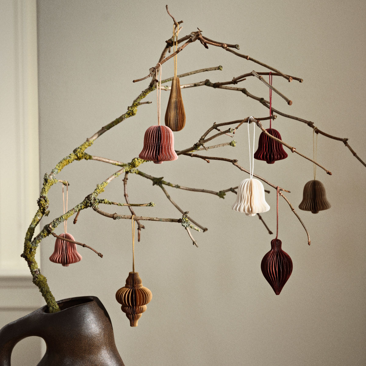 Christmas decorations hang from a branch in a vase.